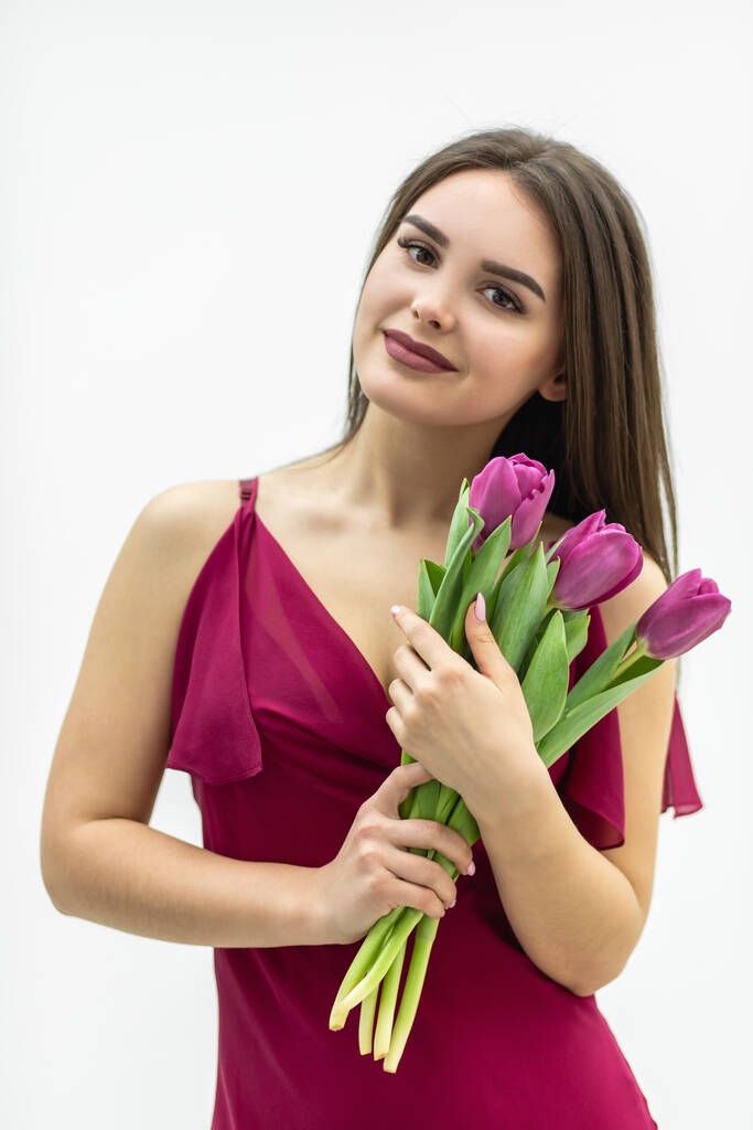Linda chica con un ramo de tulipanes se ve con placer y sonríe tiernamente. - Foto, Imagen