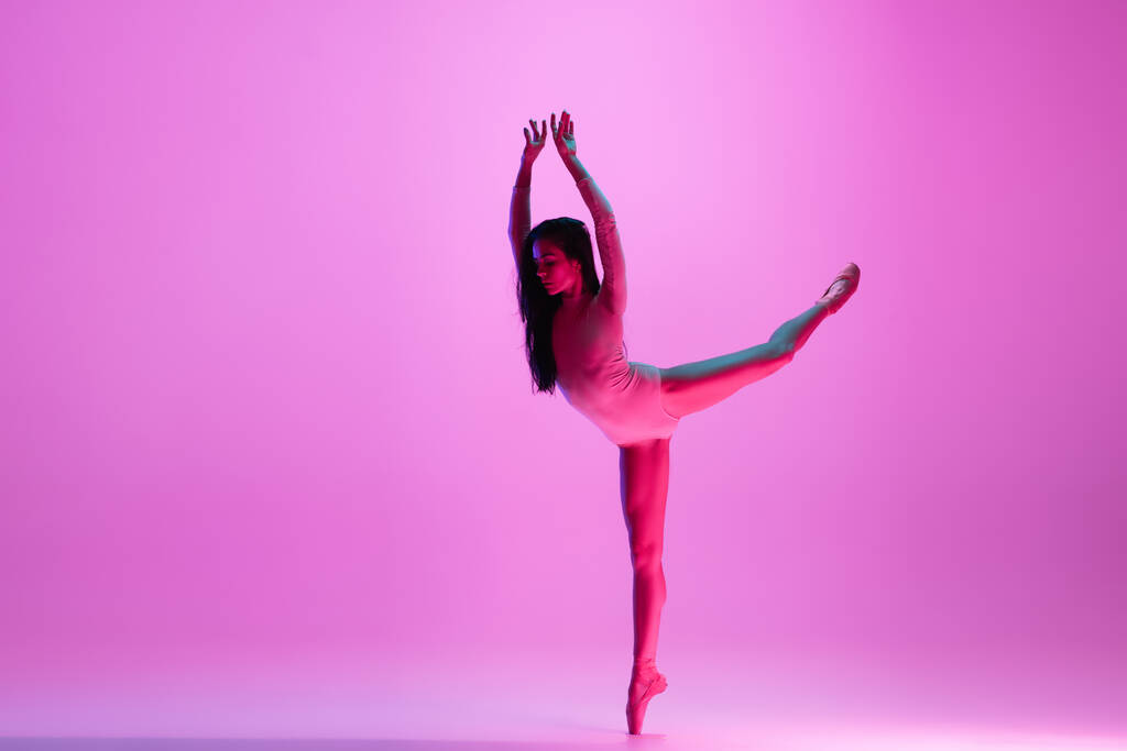 Jonge en sierlijke balletdanser geïsoleerd op roze studioachtergrond in neonlicht. Kunst, beweging, actie, flexibiliteit, inspiratie. - Foto, afbeelding