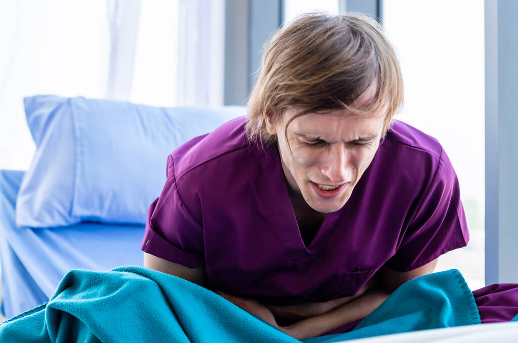 Jeune homme patient ayant eu un mal de ventre sévère couché, intoxication alimentaire sur le lit dans la chambre fond de l'hôpital. - Photo, image