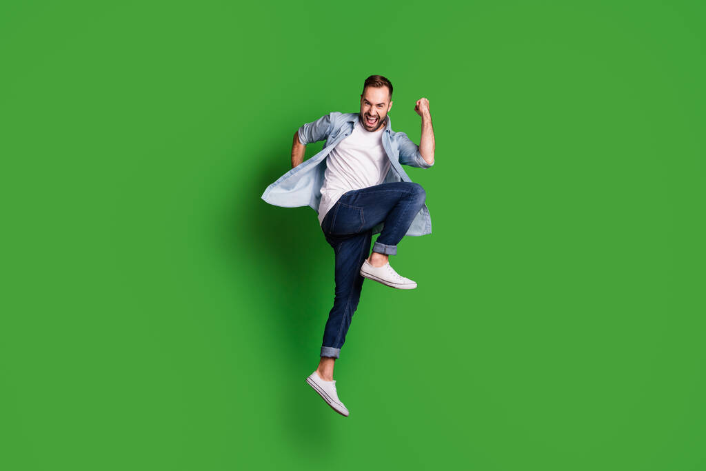 Full size profil zdjęcie imponujący funky facet skakać nosić niebieski koszula dżinsy obuwie izolowane na zielonym tle kolor - Zdjęcie, obraz