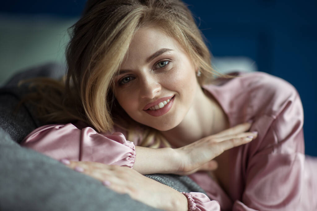 Крупный план портрета молодой красивой блондинки с волнистыми волосами в розовом пеньюаре с опускающейся шеей. Текстовое пространство - Фото, изображение