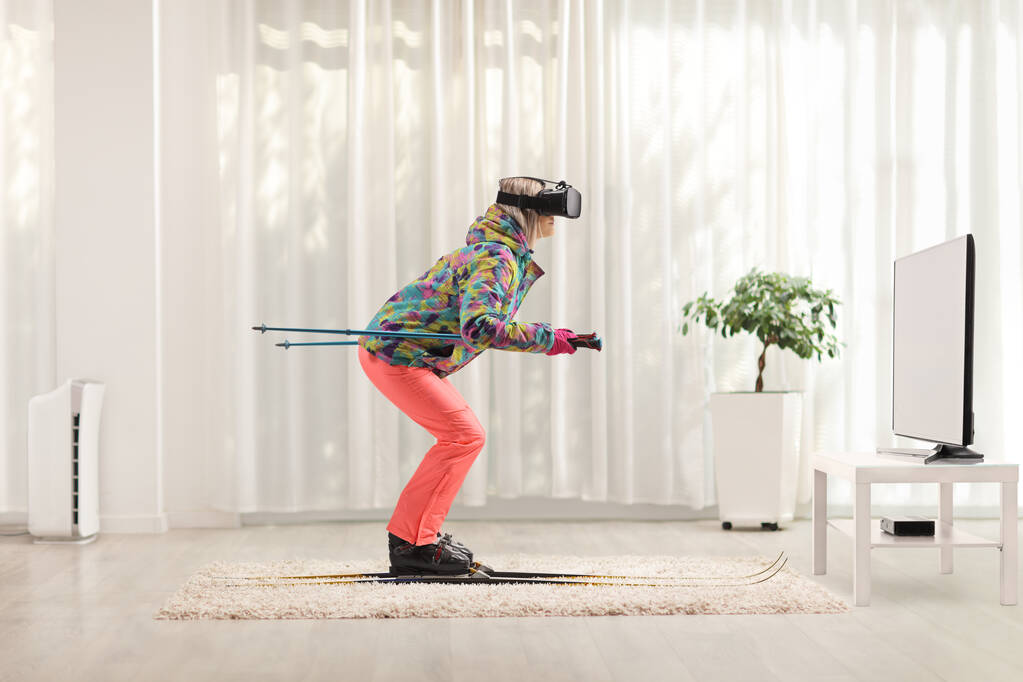Foto de perfil de longitud completa de una hembra con un auricular vr esquiando en casa  - Foto, imagen