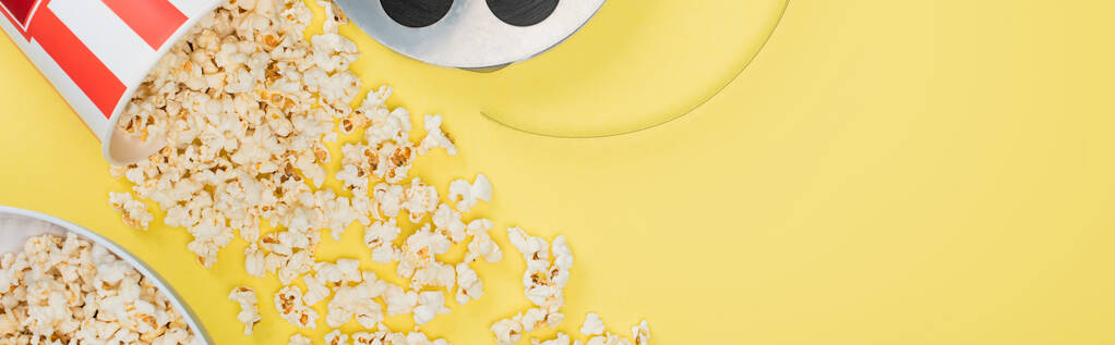 vista dall'alto della bobina del film vicino ai secchi con popcorn su giallo, banner, concetto di cinema - Foto, immagini