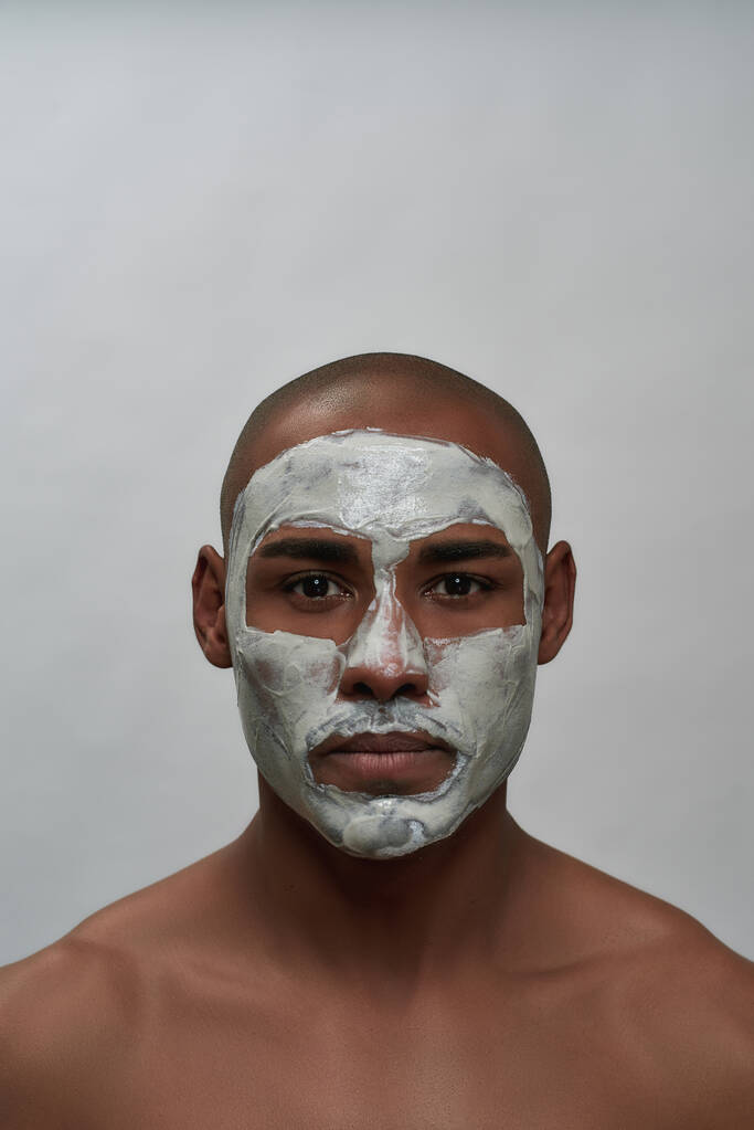 Przystojny młody Afroamerykanin patrzy w kamerę, używając maski do usuwania porów czarnej głowy, pozując na szarym tle - Zdjęcie, obraz