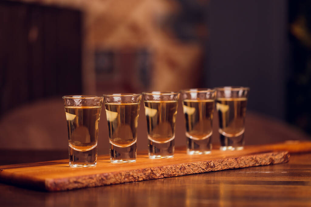 Variatie van harde alcoholische shots geserveerd op bar teller. Wazige flessen op achtergrond. - Foto, afbeelding