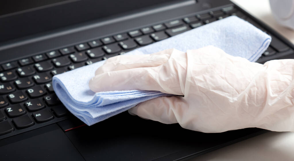 濡れた消毒用ワイプを使用してノートパソコンのキーボードを消毒手袋の女性の手。キーボードを掃除する女。新しいノーマルクリーニングラップトップはホーム表面を働かせます。長い網の旗. - 写真・画像