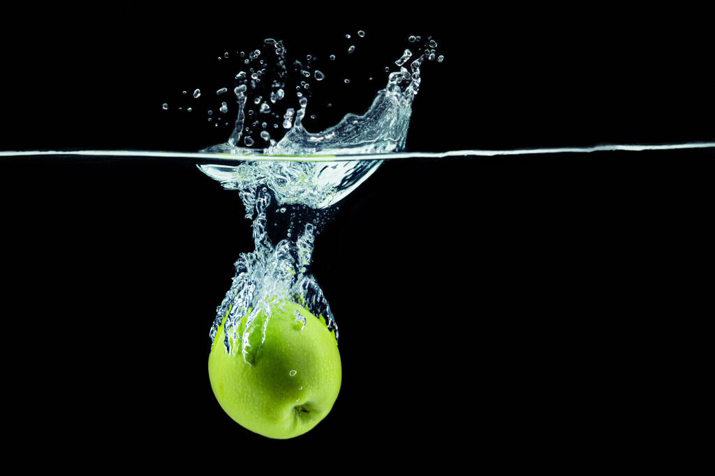 Manzana verde cayendo en el agua con un chapoteo sobre fondo oscuro - Foto, Imagen