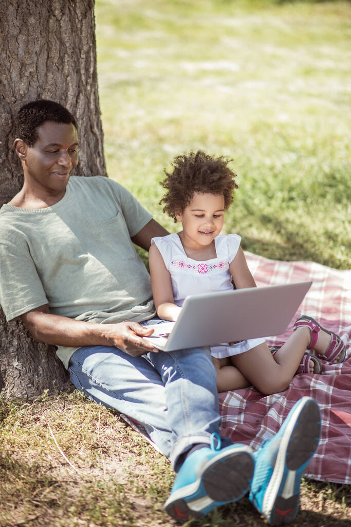 Petite fille aux cheveux bouclés et son père regardant quelque chose sur ordinateur portable - Photo, image