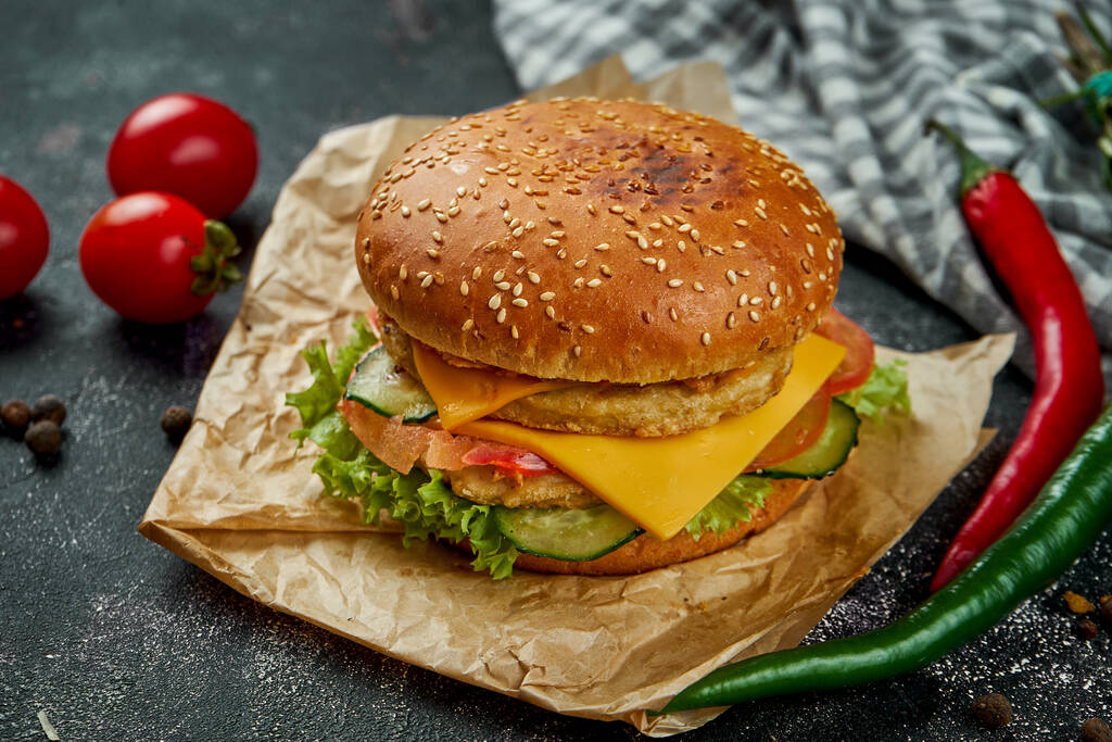 Sappige dubbele hamburger met kip, tomaten, kaas en knapperige uien op een donkere achtergrond. Kippenburger - Foto, afbeelding