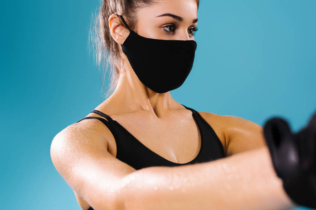 Обрезанное фото концентрированной девушки в защитной маске на синем фоне. Спорт, здоровый образ жизни и пандемия. - Фото, изображение