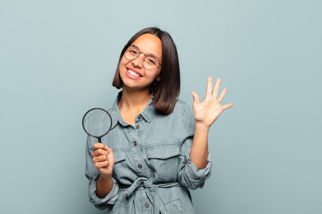 νεαρή Ισπανίδα που χαμογελά και δείχνει φιλική, δείχνοντας νούμερο πέντε ή πέμπτη με το χέρι μπροστά, μετρώντας αντίστροφα - Φωτογραφία, εικόνα