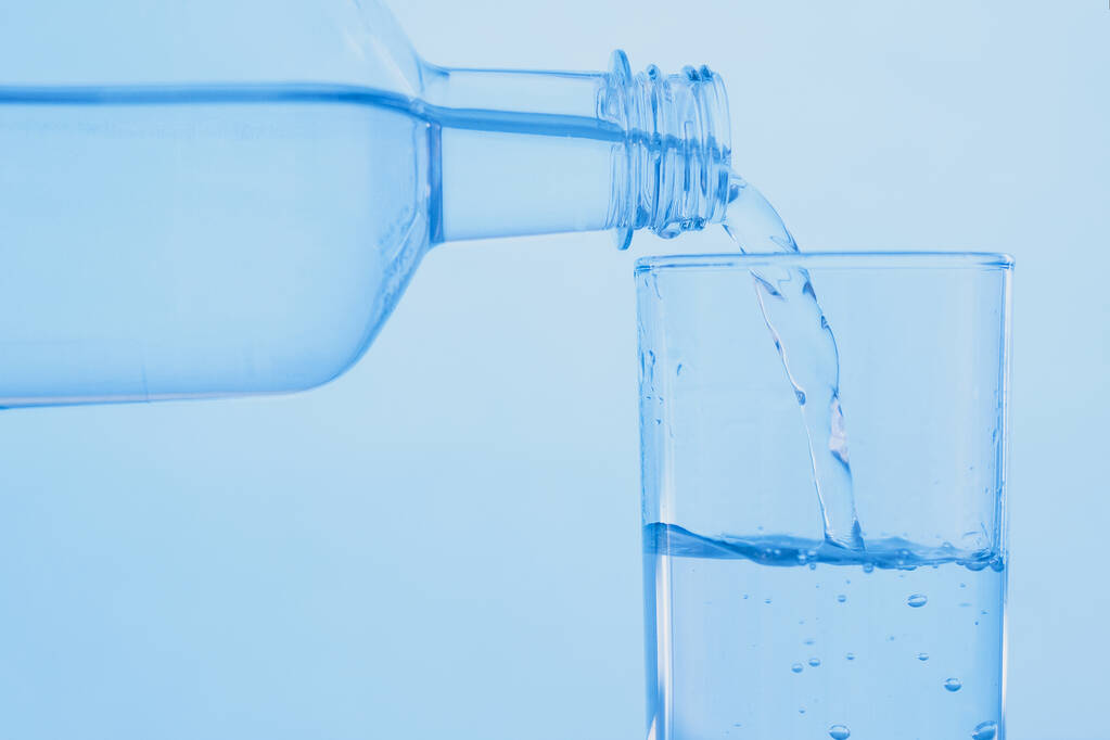 Aus einer durchsichtigen Flasche wird Wasser in ein Glas gegossen. Das Konzept des Weltwassertages. - Foto, Bild