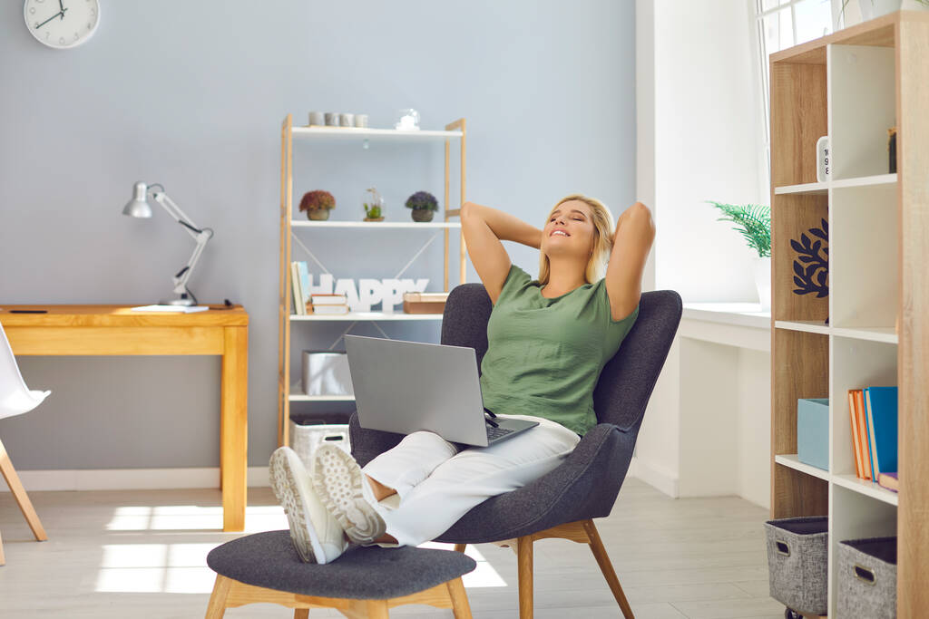 Jeune femme assise sur des chaises dans une position confortable dans le bureau avec ordinateur portable et relaxant - Photo, image
