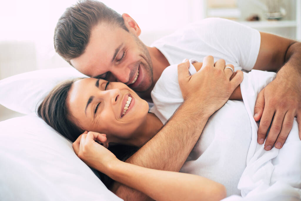 Feliz linda joven hermosa pareja enamorada abrazándose y divirtiéndose en la gran cama blanca después del sueño - Foto, imagen