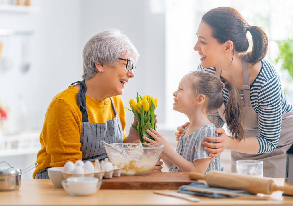 Feliz familia amorosa están preparando la panadería juntos. Niña está dando flores a su abuela en la cocina.  - Foto, imagen