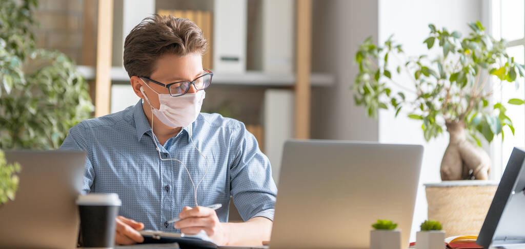Jongeman met gezichtsmasker werkt aan een laptop op kantoor.. - Foto, afbeelding