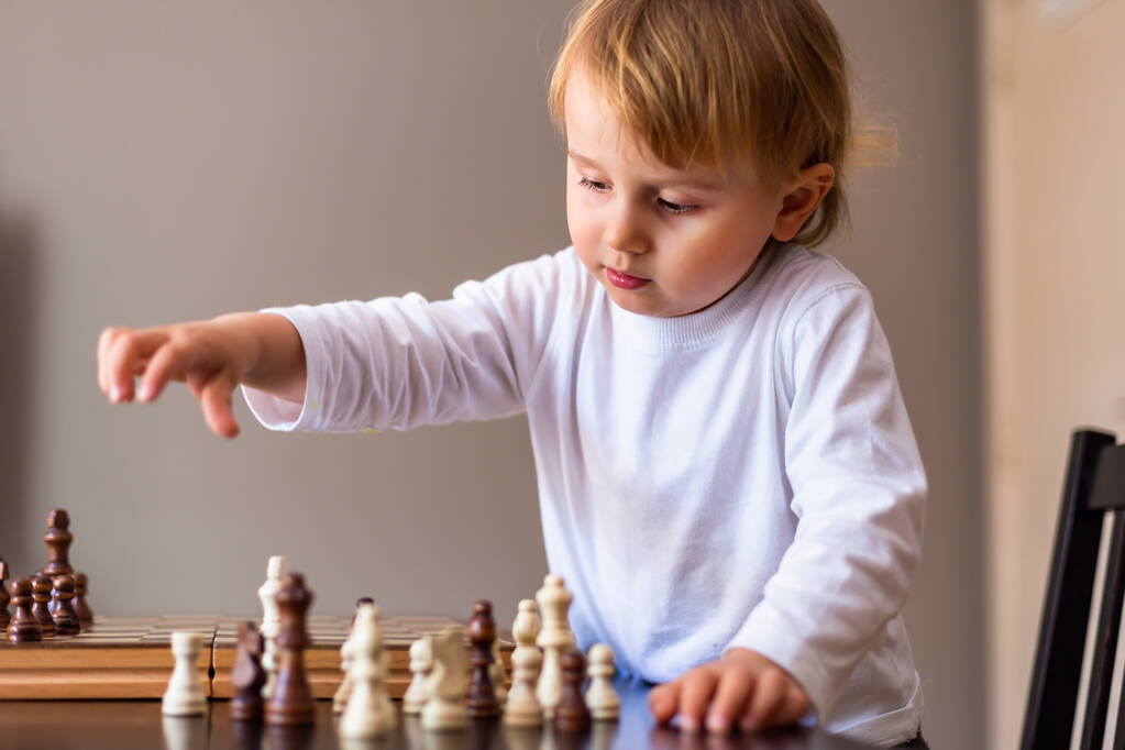 El niño aprende a jugar al ajedrez. Niño sentado en la mesa en casa cerca del tablero de ajedrez. Educación temprana de ajedrez. - Foto, Imagen
