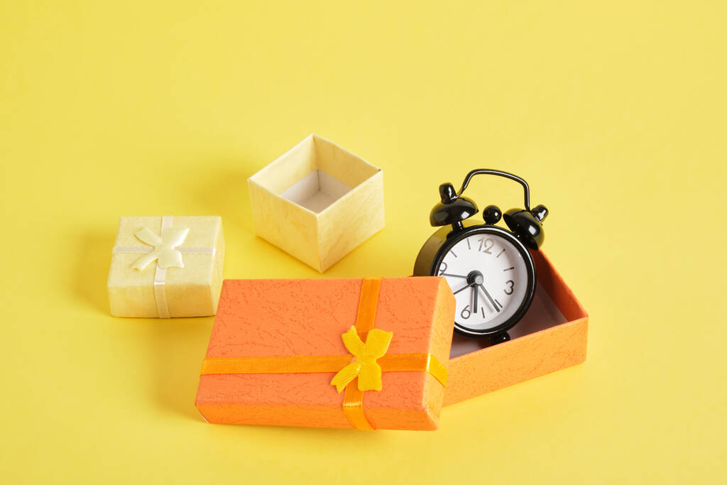 ブラックレトロな目覚まし時計とギフトボックス黄色の背景コピースペース。お祝いの時間の概念 - 写真・画像