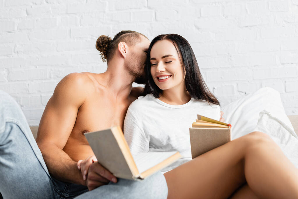sexy mężczyzna całuje uśmiechnięta dziewczyna z książki na zamazany pierwszy plan  - Zdjęcie, obraz