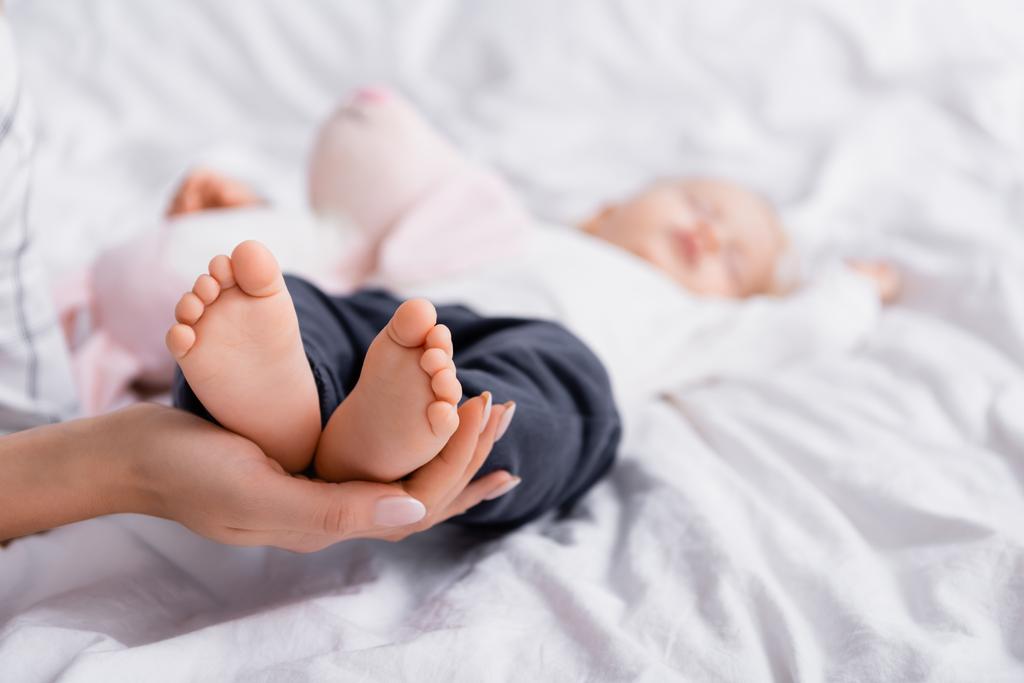 femme touchant les pieds du petit fils dormant sur une literie blanche, fond flou - Photo, image