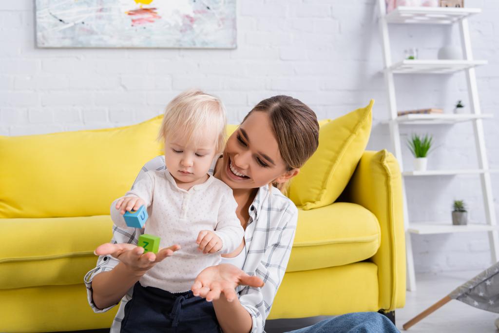 iloinen nainen tilalla lelu kuutio lähellä pieni poika kotona - Valokuva, kuva