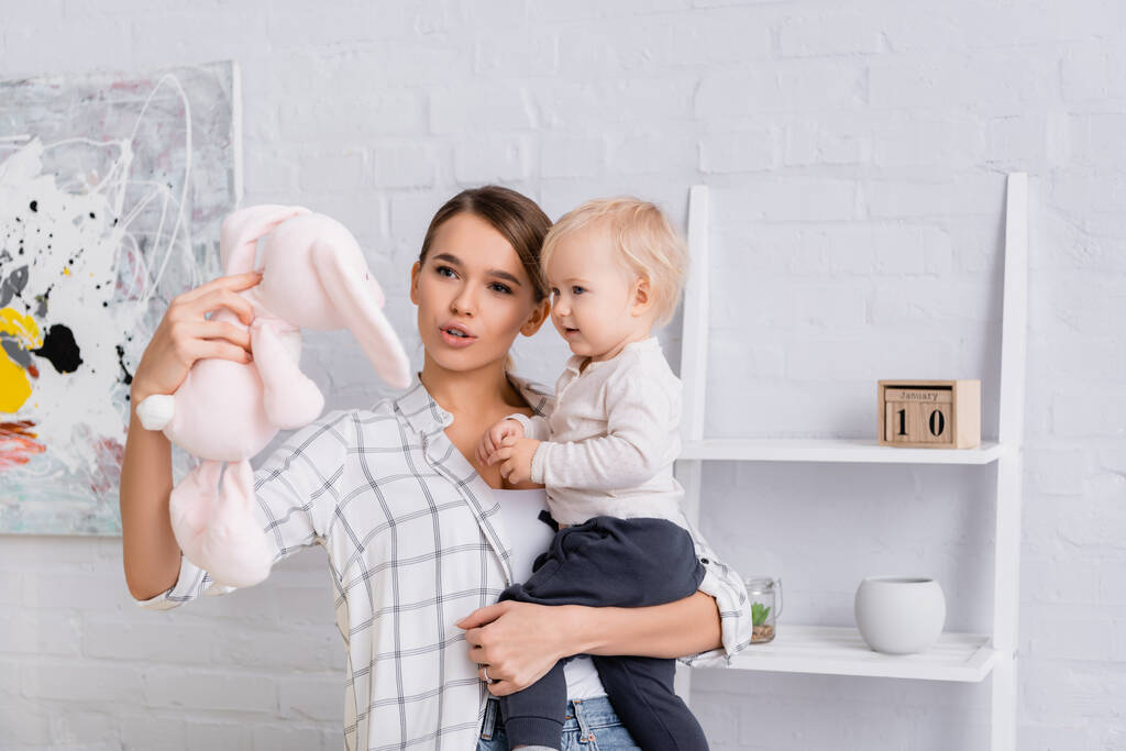 giovane madre tenendo bambino ragazzo e coniglietto giocattolo a casa - Foto, immagini