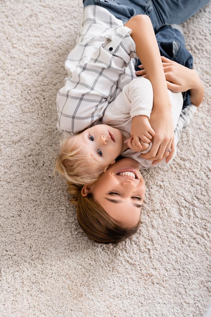 shora pohled na radostnou ženu objímající syna, jak spolu leží na podlaze - Fotografie, Obrázek