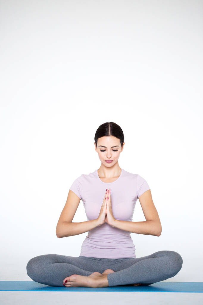 Beautiful young woman in sportswear practicing yoga while sitting in lotus position on white background. Namaste. - Photo, Image