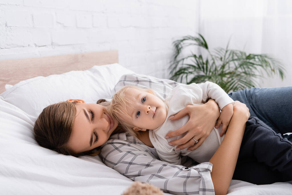 młoda kobieta przytula małe dziecko leżąc razem na łóżku - Zdjęcie, obraz