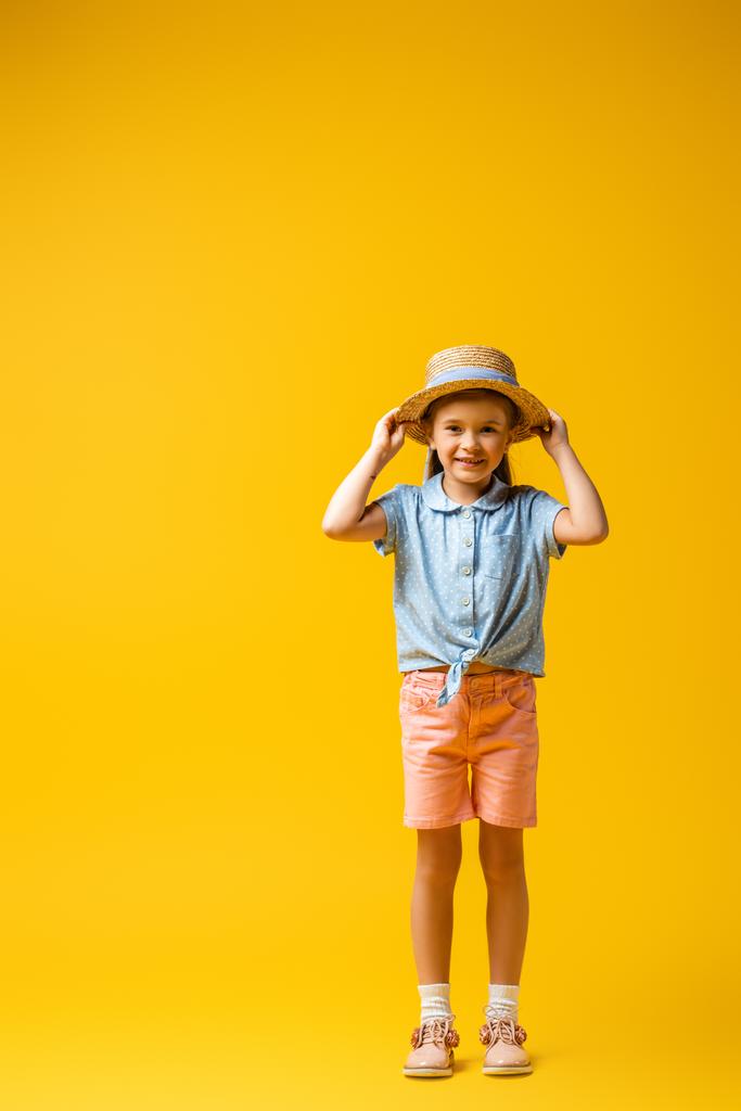 黄色の上に藁帽子を調整する幸せな子供の完全な長さ - 写真・画像