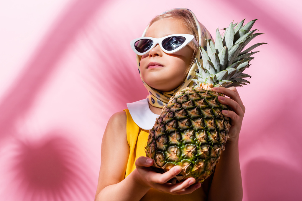 fille en foulard et lunettes de soleil tenant l'ananas sur rose  - Photo, image