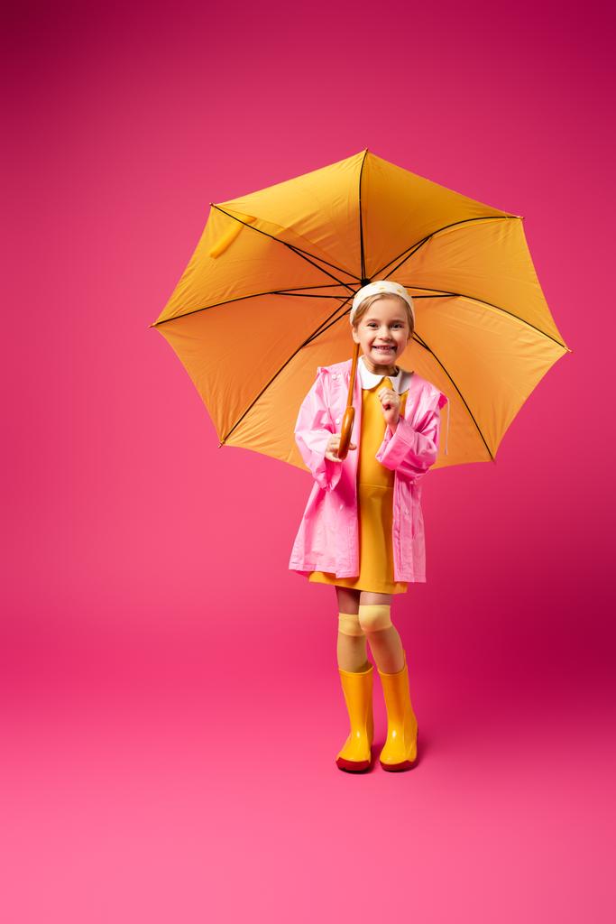 Sarı şemsiye altında kırmızı yağmurluk giyen mutlu bir kız. - Fotoğraf, Görsel