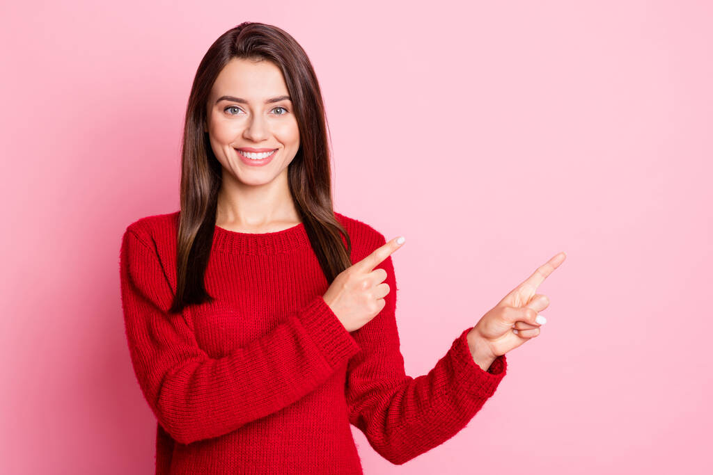 Retrato fotográfico de una simpática jovencita vestida con ropa roja sonriendo señalando el espacio vacío con los dedos de ambas manos aislados sobre un fondo de color rosa - Foto, Imagen