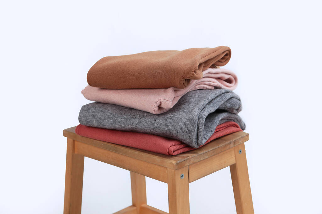 Gebreide wollen kleding ligt op een houten stoel. Kleding gemaakt van natuurlijke wol voor het koude seizoen. Lichte achtergrond. Geen mensen.. - Foto, afbeelding