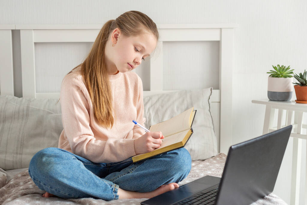 Teinityttö tekee kotiläksyjä sängyllä kotona. Sosiaalinen etäisyys, itsensä eristäminen - Valokuva, kuva