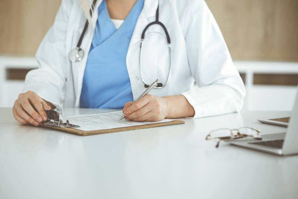 Mujer médica desconocida en el trabajo llenando el formulario de registro de historial de medicamentos en la clínica, primer plano del portapapeles - Foto, imagen