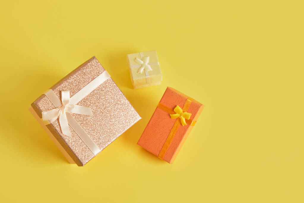 tres cajas de regalo de diferentes colores, tamaños y formas sobre un fondo amarillo, rosa, amarillo y naranja cajas de regalo vista superior - Foto, Imagen