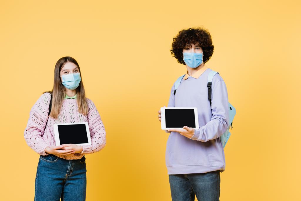Teini-ikäiset lääketieteellisissä naamioissa, joilla on digitaalisia tabletteja, joissa on tyhjä näyttö keltaisella taustalla - Valokuva, kuva
