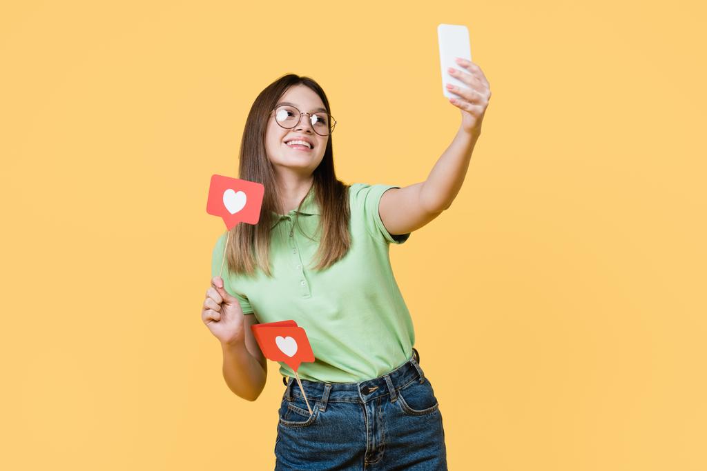 Fröhlicher Teenager hält Papierherz am Stock und macht Selfie isoliert auf gelb - Foto, Bild