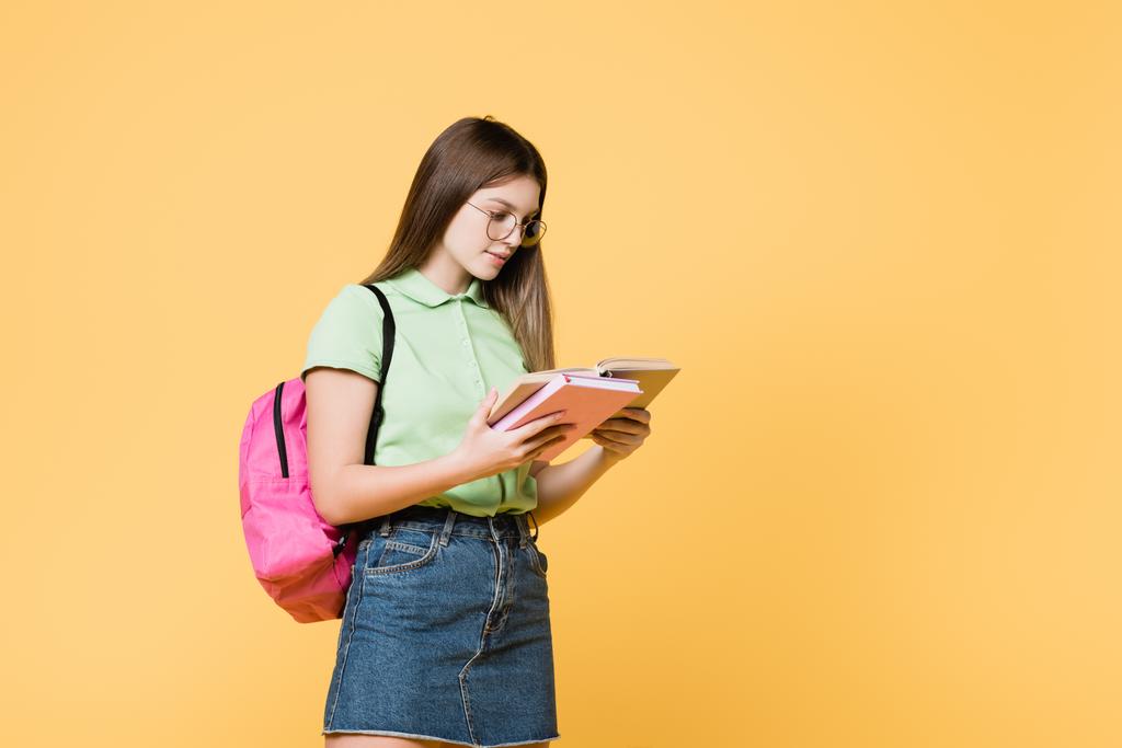 Chica en gafas con mochila libro de lectura aislado en amarillo - Foto, Imagen