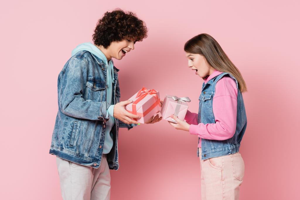 Εντυπωσιακό ζευγάρι εφήβων κοιτάζοντας τα δώρα σε ροζ φόντο  - Φωτογραφία, εικόνα