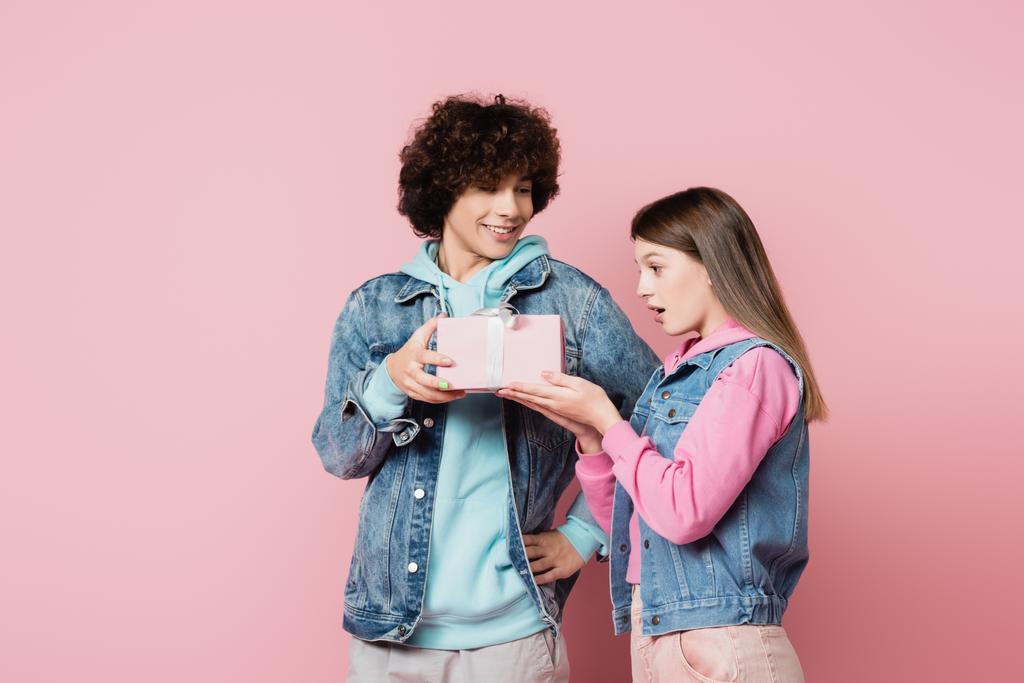 Usmívající se teenager dávat dárek vzrušené přítelkyně na růžovém pozadí  - Fotografie, Obrázek