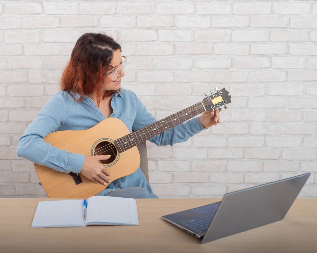 Μια γυναίκα μαθαίνει να παίζει κιθάρα στο διαδίκτυο. Μάθημα απομακρυσμένης μουσικής - Φωτογραφία, εικόνα