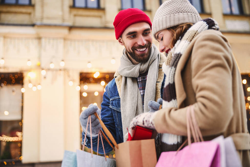 Χαρούμενος γενειοφόρος άντρας πηγαίνει για ψώνια με την κοπέλα του το χειμώνα. - Φωτογραφία, εικόνα