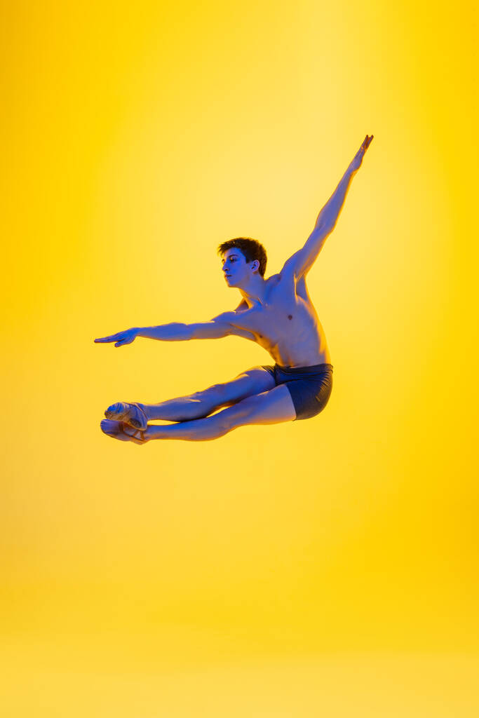 Giovane e graziosa ballerina isolata su sfondo giallo studio in luce al neon. Arte, movimento, azione, flessibilità, concetto di ispirazione. - Foto, immagini