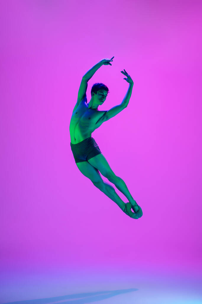 Jeune et gracieux danseur de ballet isolé sur fond de studio violet sous la lumière du néon. Art, mouvement, action, flexibilité, concept d'inspiration. - Photo, image