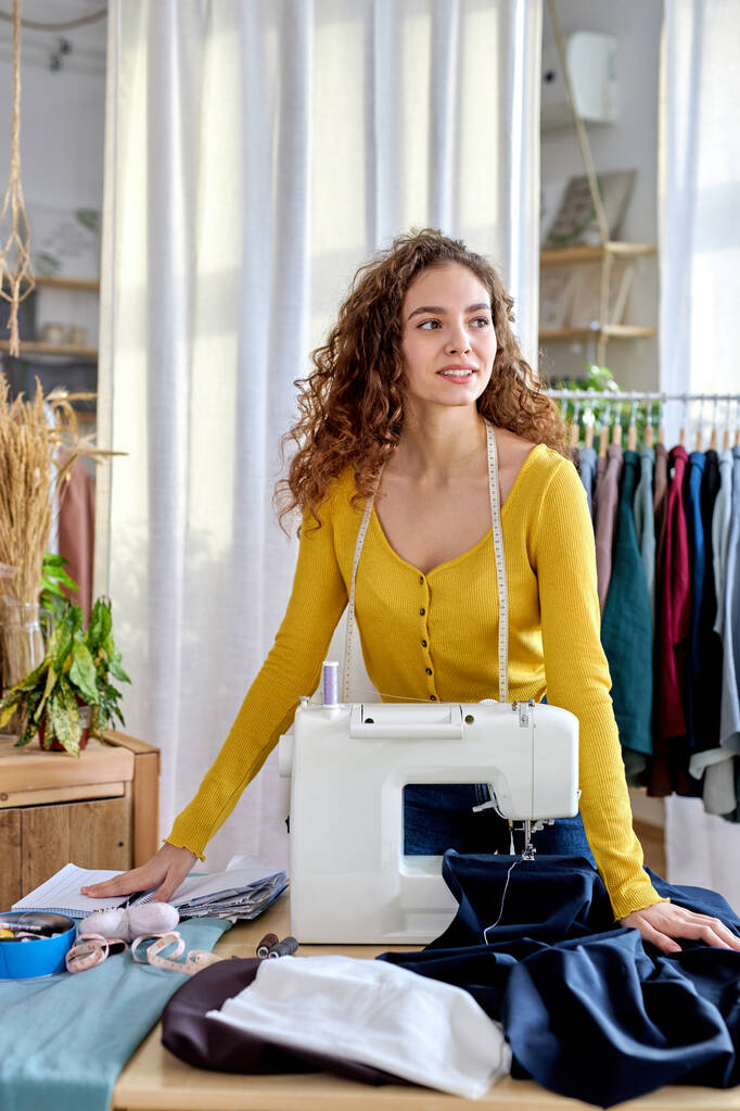 profesjonalna urocza młoda projektantka odzieży stojąca przy maszynie do szycia w pracowni - Zdjęcie, obraz