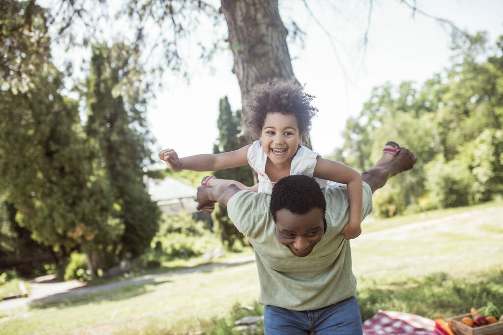 Αφρο-αμερικάνος πατέρας και η κόρη του περνάνε καλά μαζί στο πάρκο και νιώθουν χαρούμενοι. - Φωτογραφία, εικόνα