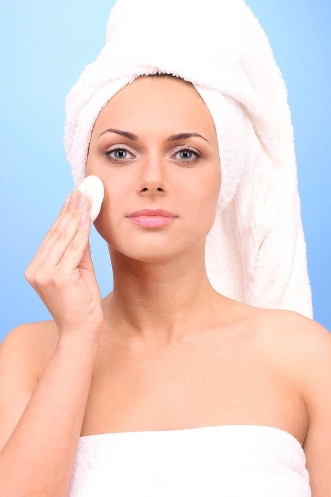 Beautiful young woman after shower with a towel on her head and a cotton pad in hand on blue background close-up - Photo, Image