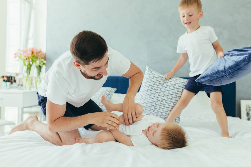 husband father playing with his children, two little boys brothers, in a large bedroom - Photo, Image
